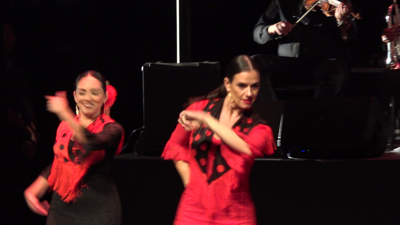 Two dancers in red and black costumes on a dark stage.
