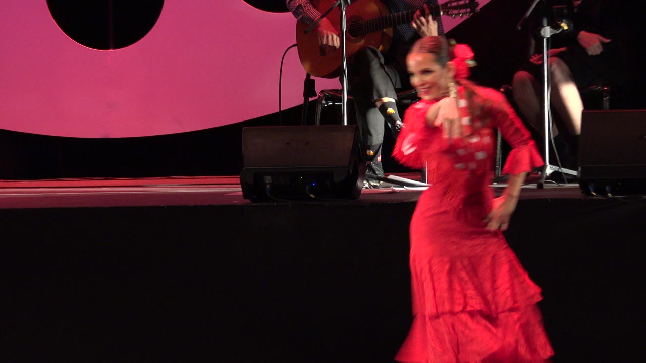 Red-dressed dancer on a stage with musicians behind her.