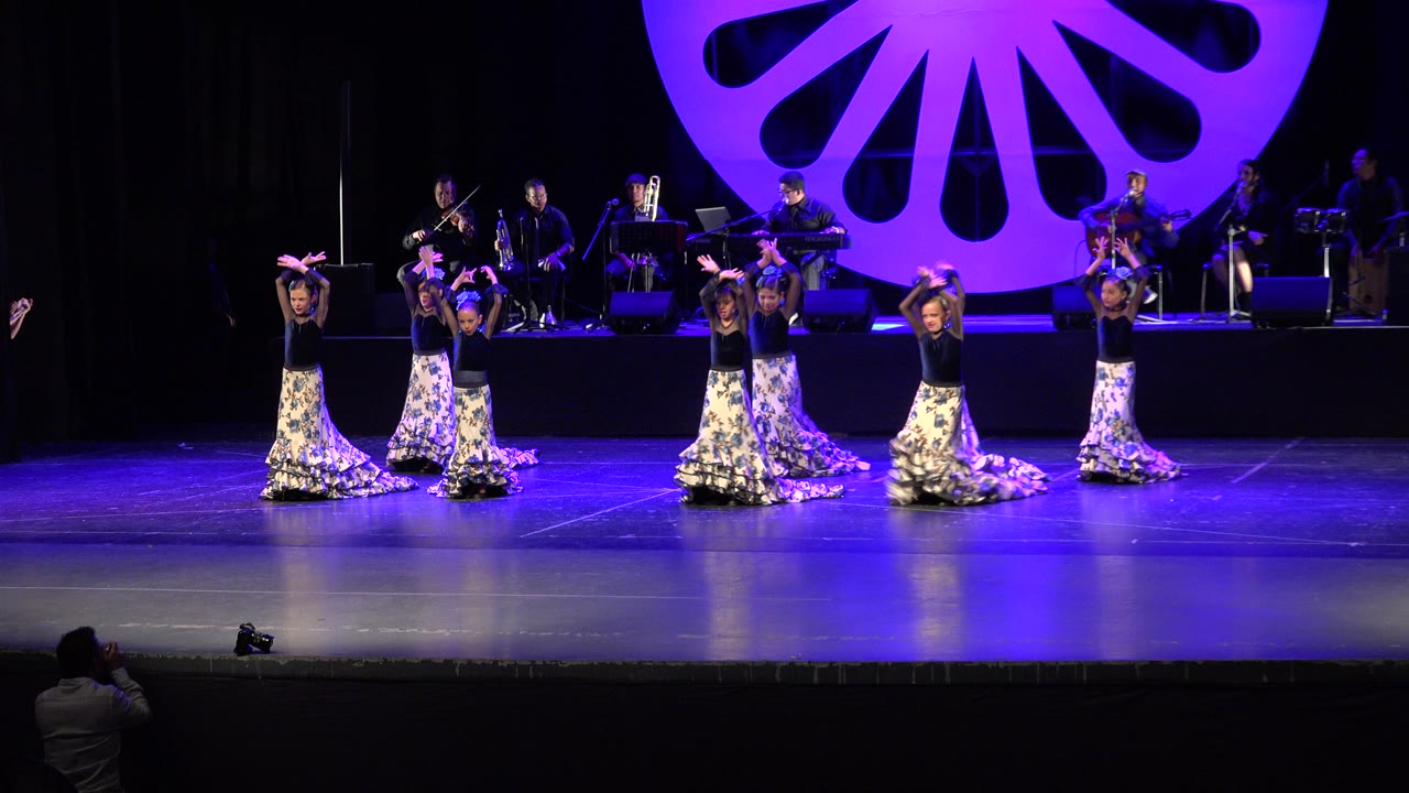 Wide stage view of dancers performing under blue and purple lighting.