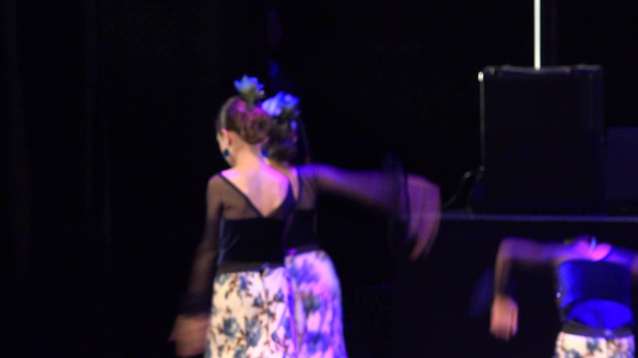 Several child dancers move across the Cabo San Lucas stage, including a child in a black top and another blurred dancer entering from the right.