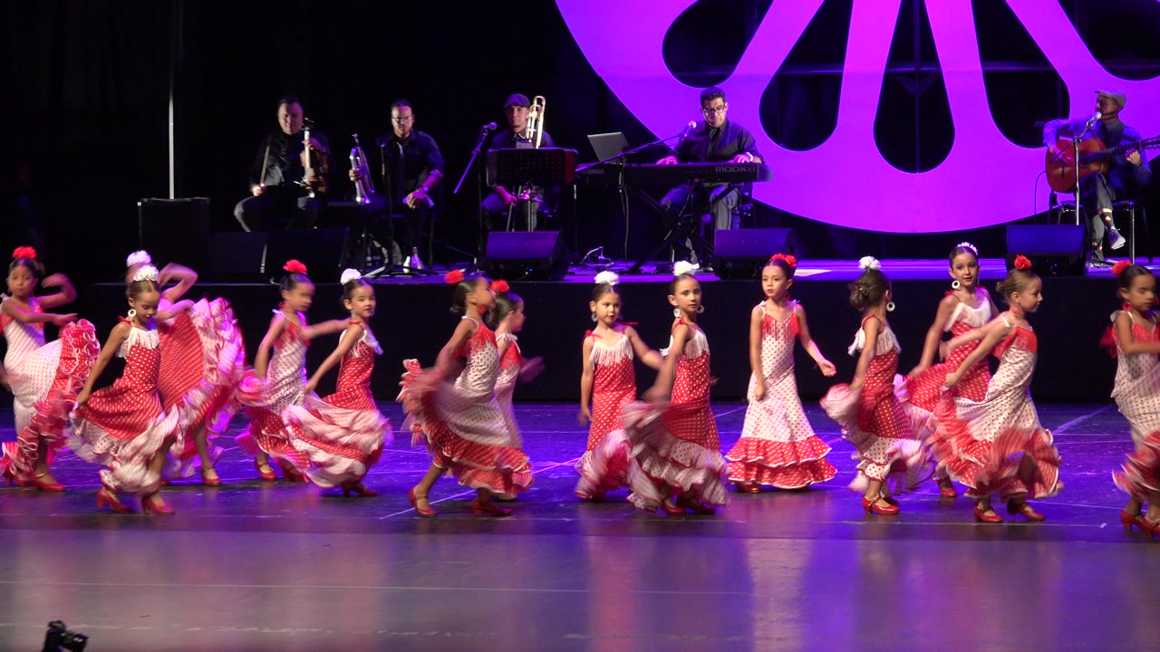 The dancers continue across the Cabo San Lucas stage, with skirts lifted in motion and the musicians still seated behind the performance line.