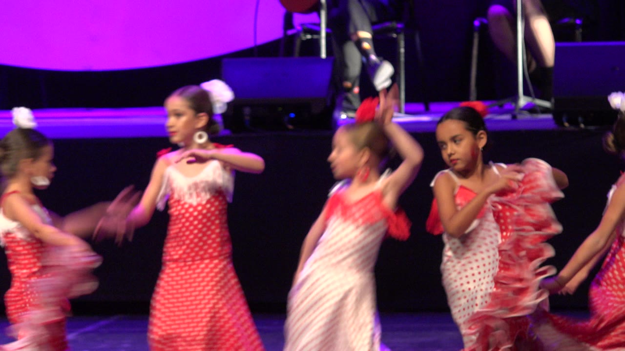 Young girls in red and white dance costumes performing on a purple-lit stage.