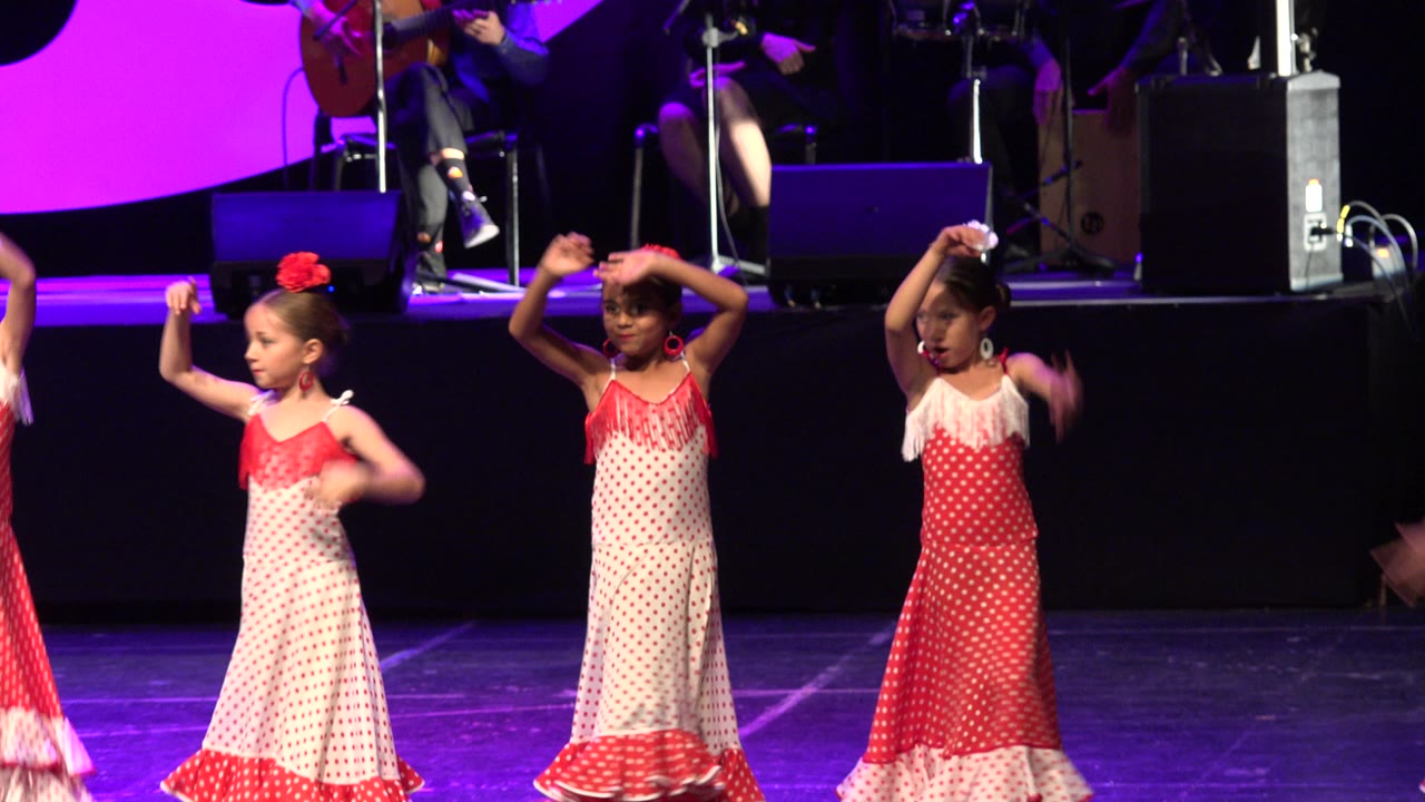 Three young girls dancing in red and white dresses on a lit stage.