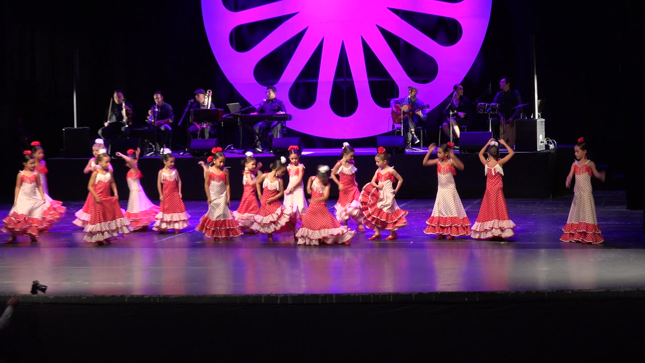 In Cabo San Lucas, Mexico, the young dancers shift positions across the stage, with several girls facing forward and others turning near the purple floral backdrop.