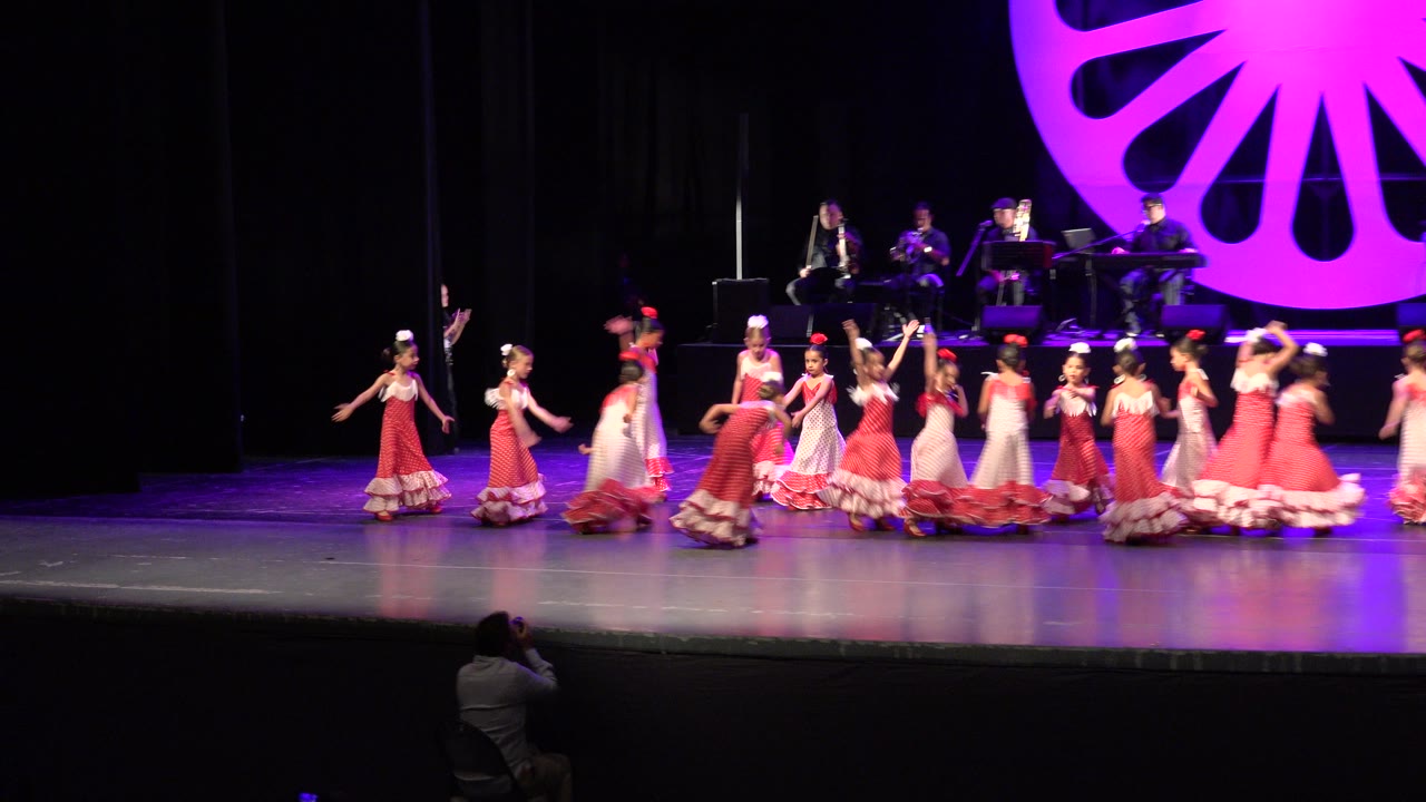 Girls in red and pink dresses dancing on a theater stage.