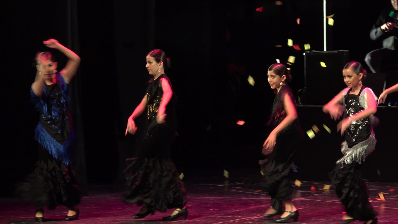 Children in black and blue dance outfits performing under pink stage light.