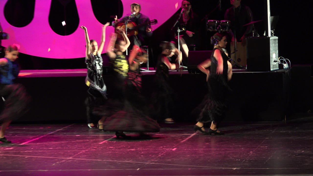 Dancers moving across a stage with musicians behind them.