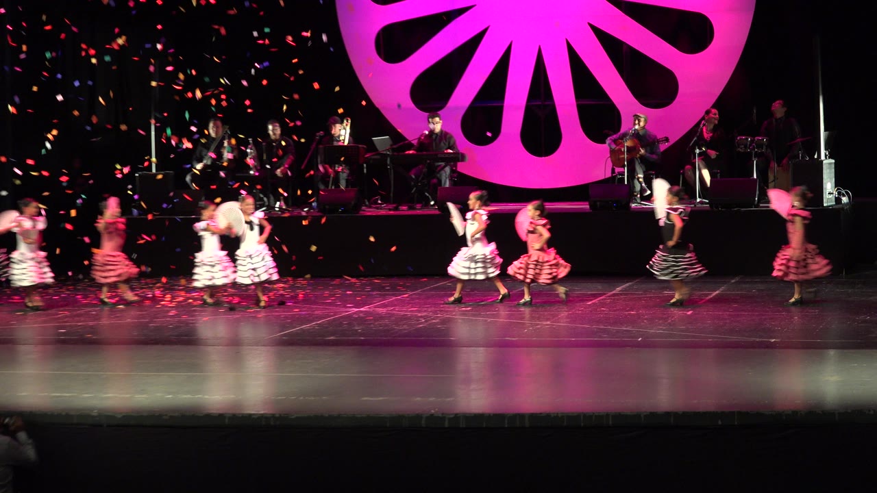 Children dance on a stage with fans and live musicians behind them.