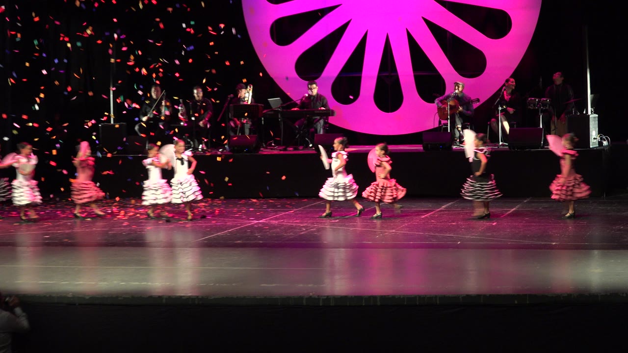 In Cabo San Lucas, Mexico, several girls spread across the stage with fans raised as the band remains visible on the rear platform under pink lighting.