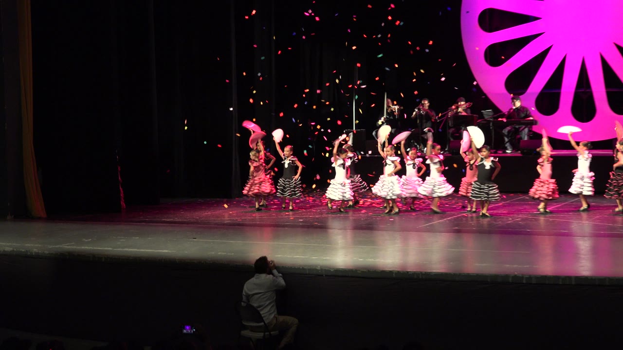 Children dancing on a stage as confetti falls.