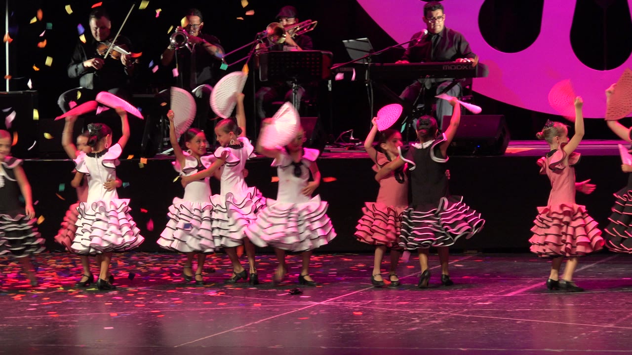 Children continue the stage routine with fans raised under pink lighting.