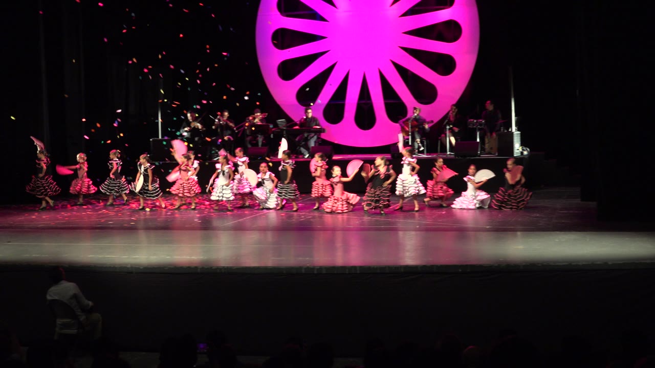 Children in patterned dance dresses cluster near center stage.