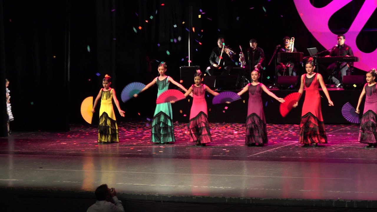 Young dancers lower and spread their fans during a stage routine.
