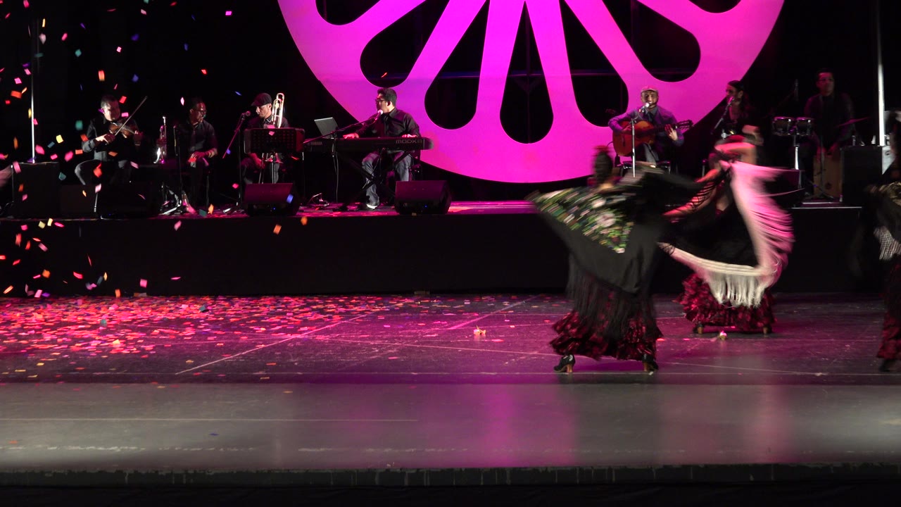 Multiple dancers spin with scarves under confetti.