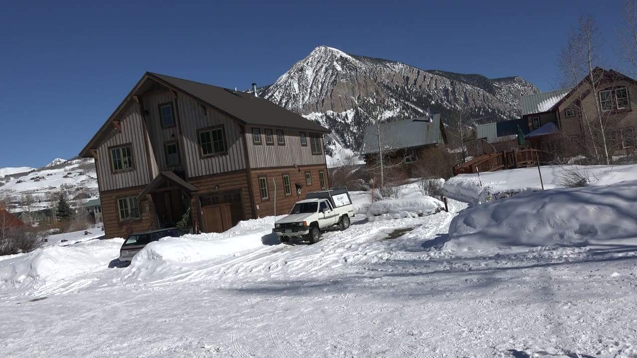 Snowy house exterior with a white truck and mountain backdrop.