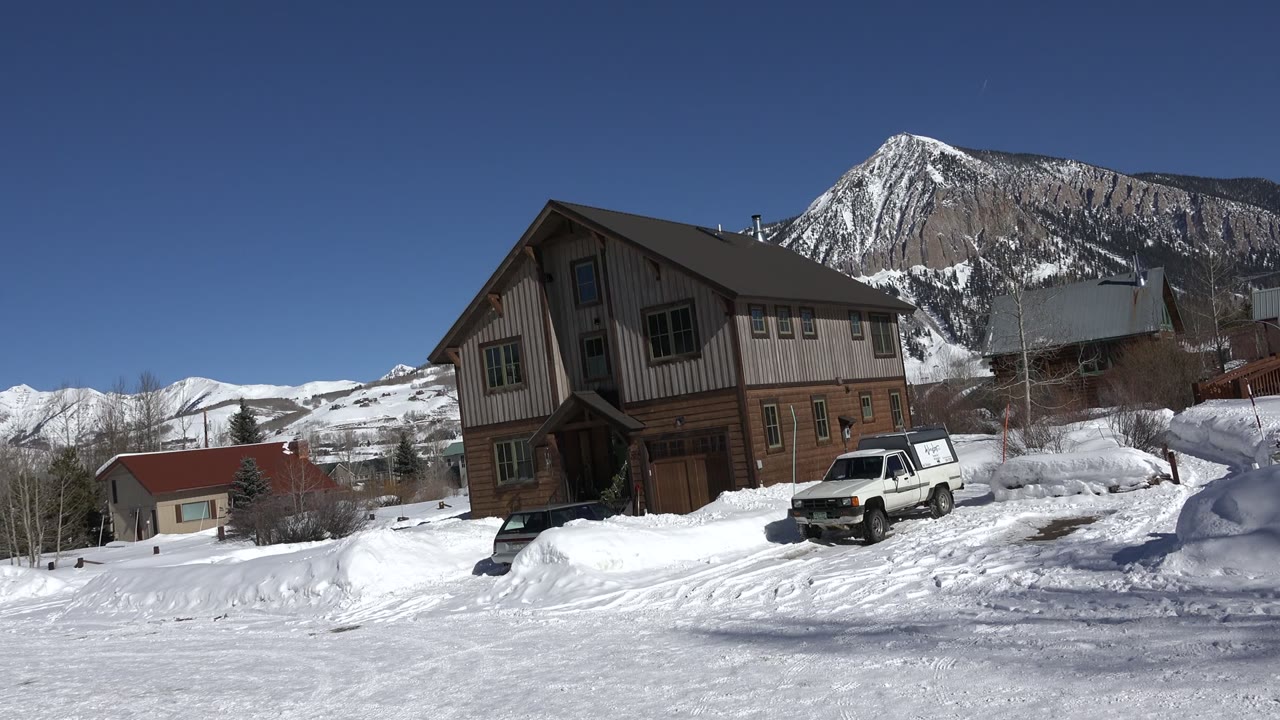 Second frame shows the Crested Butte cabin held in a similar composition, with packed snow in front, a white vehicle near the door, and no visible people.