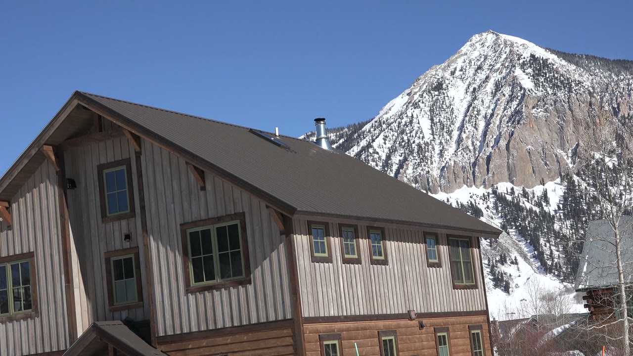 Wood cabin roof and windows in front of a snowy mountain