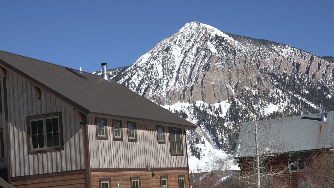 Snowy mountain behind wood-sided buildings under a blue sky.
