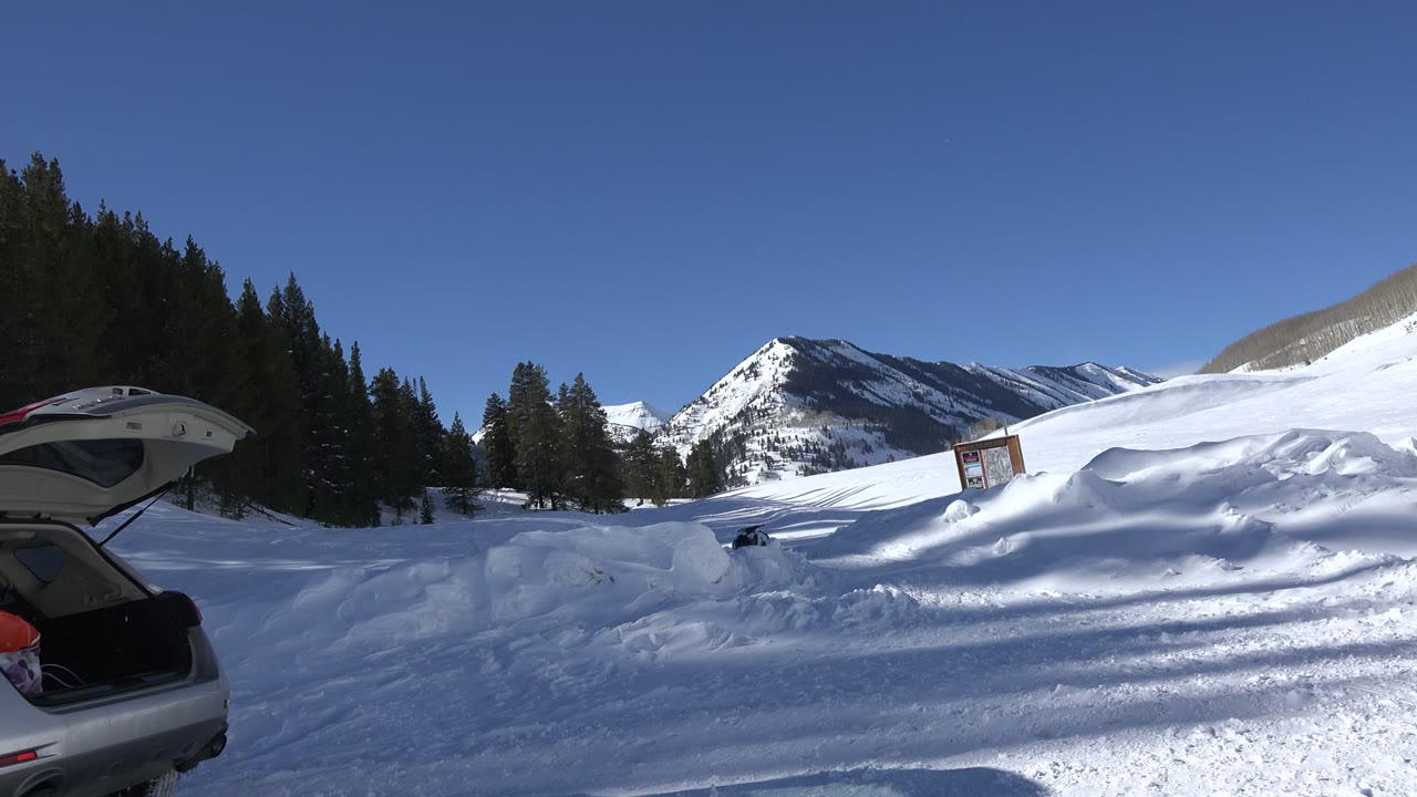 Snowy mountain landscape with an open car hatch at left.