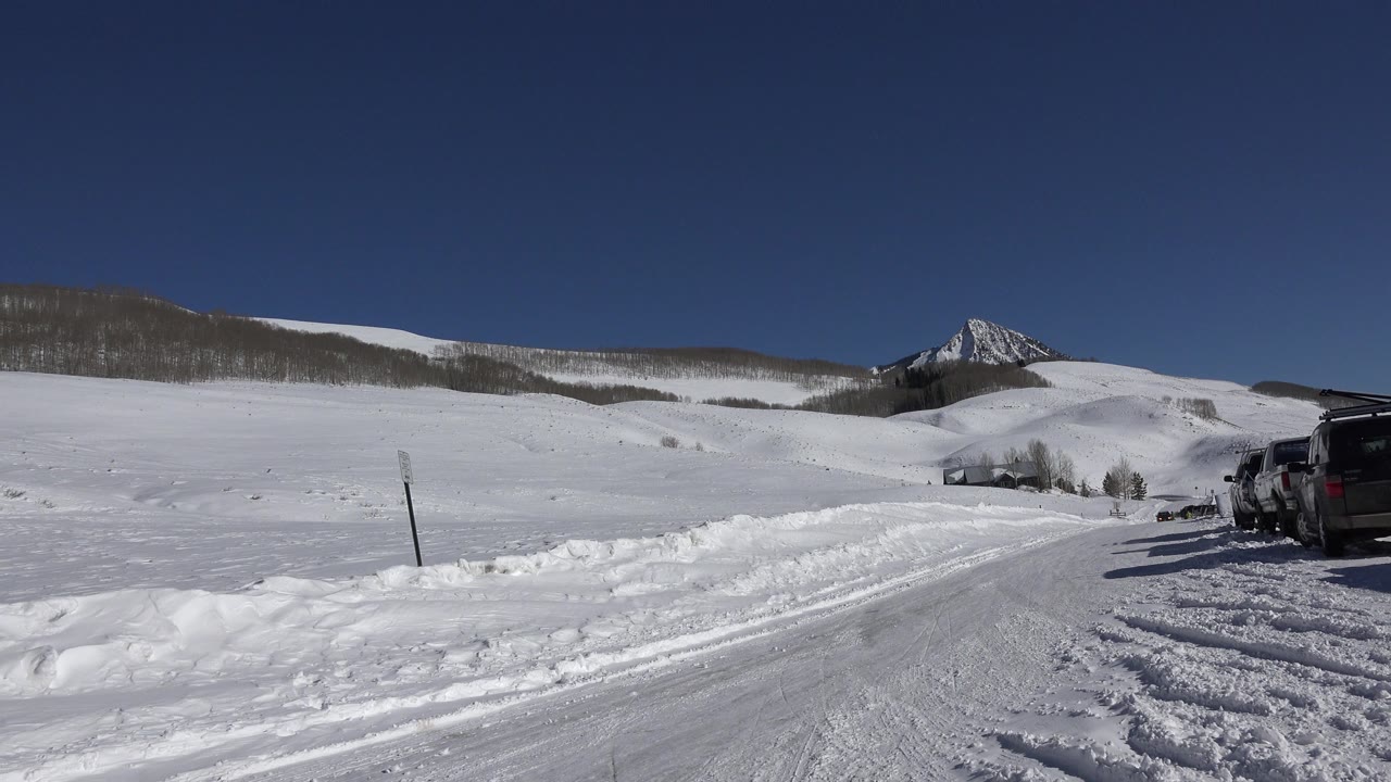 Snowy mountain road with parked vehicles and open hills