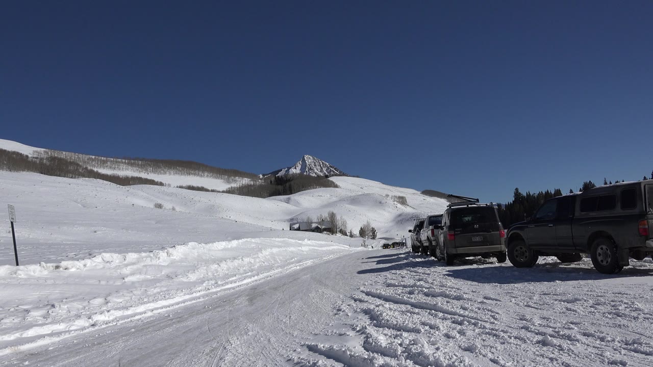 Snowy road with parked trucks and a mountain peak in the distance.
