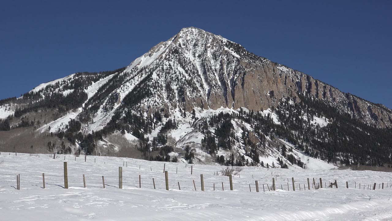Snow-covered ground and fence posts beneath a large mountain peak.