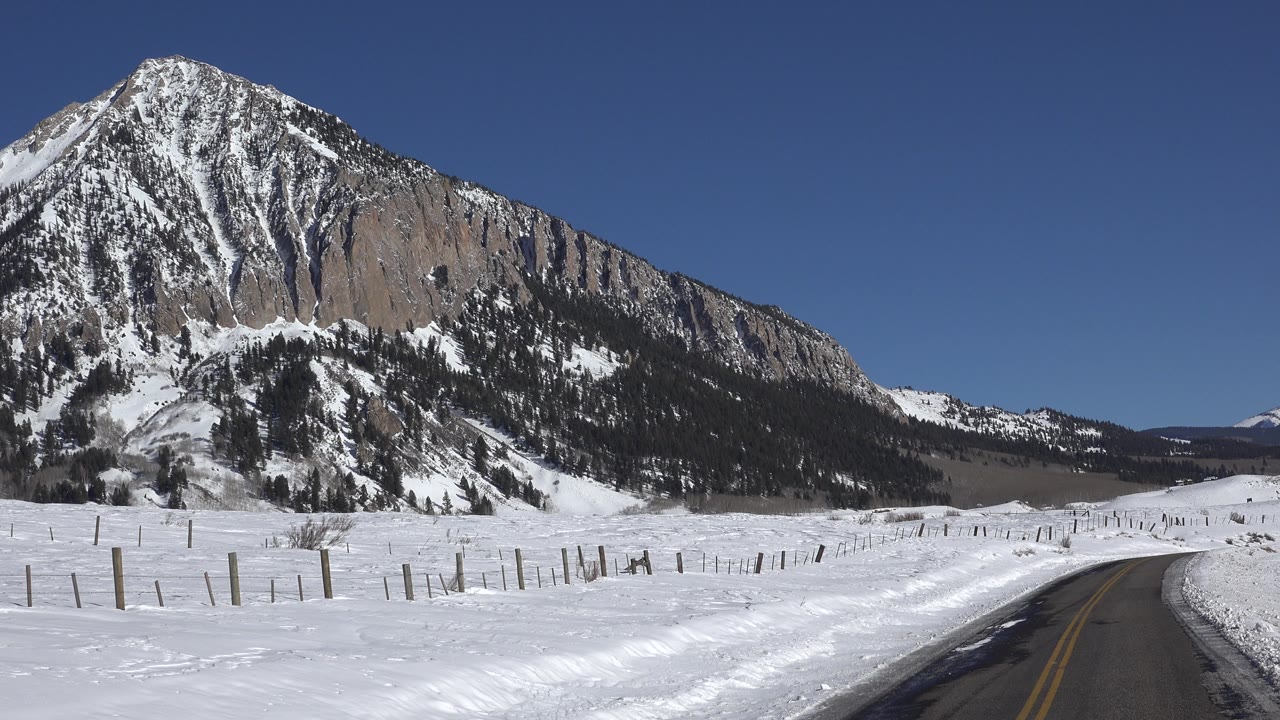 Snowy roadside and mountain under clear sky.