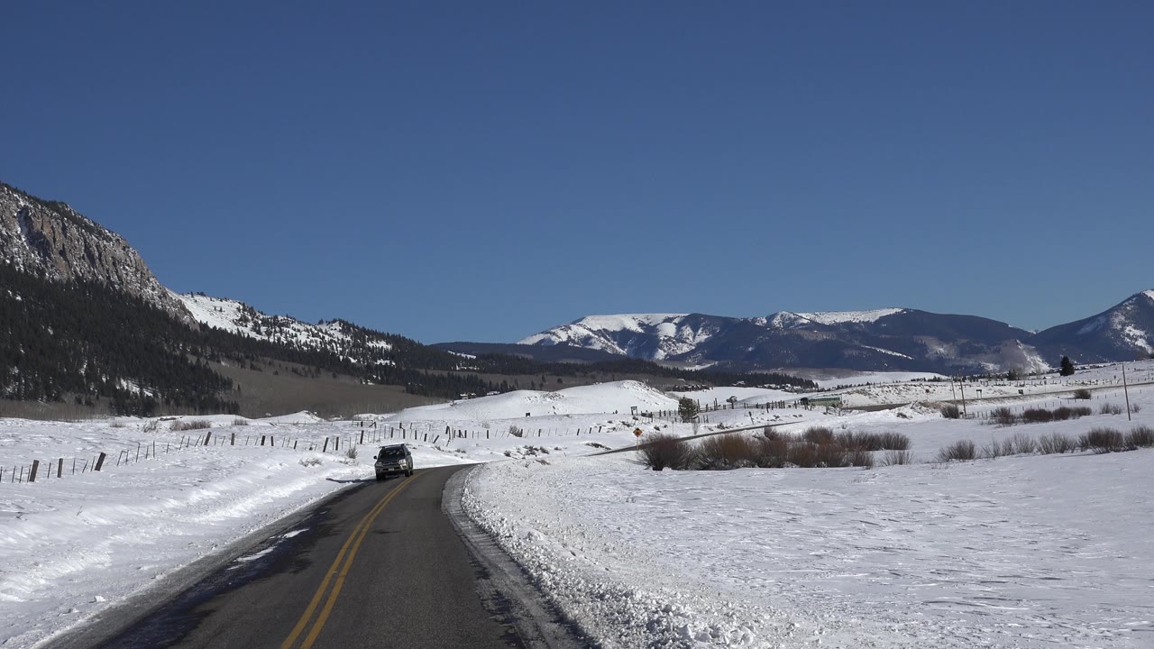 Snowy fields and mountain ridge beside a rural road.