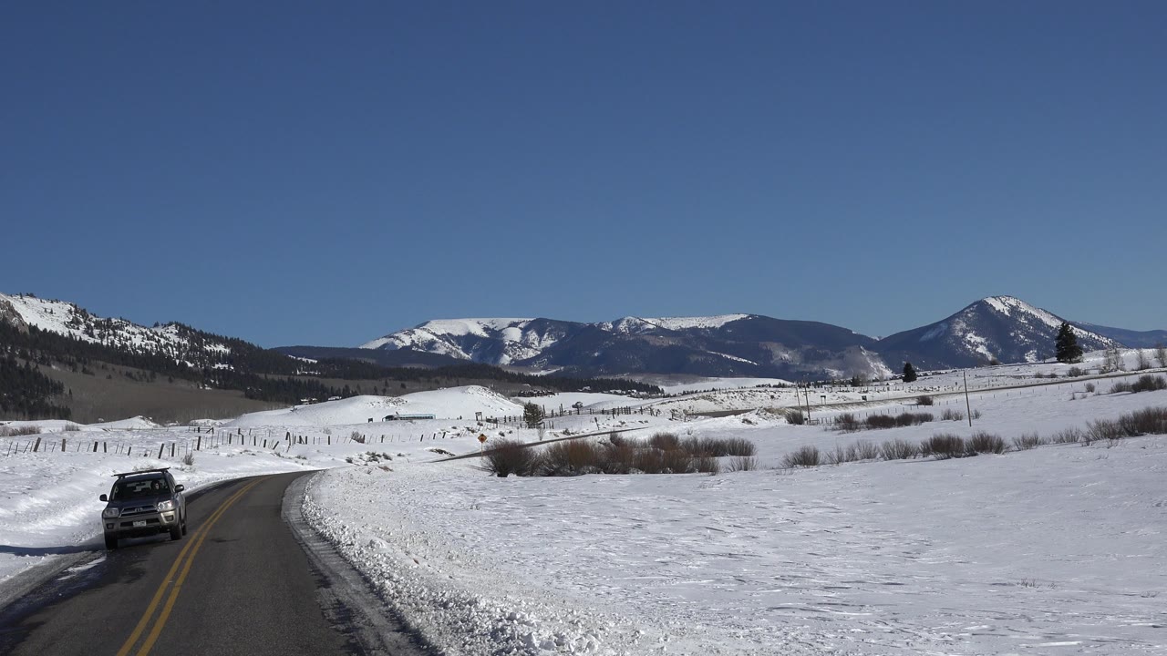 Snowy mountain road with a dark SUV approaching on the left.