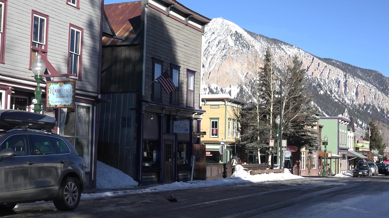 Sunlit Crested Butte street with parked cars and snowy mountain backdrop.