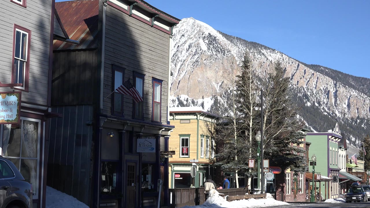 Winter village street with storefronts and a snow-covered mountain behind it.