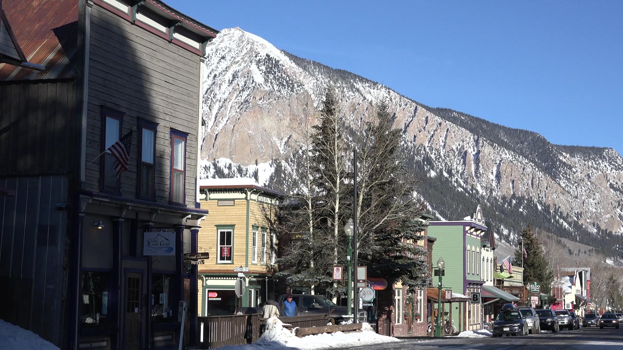 Storefront-lined winter street below a snowy mountain.