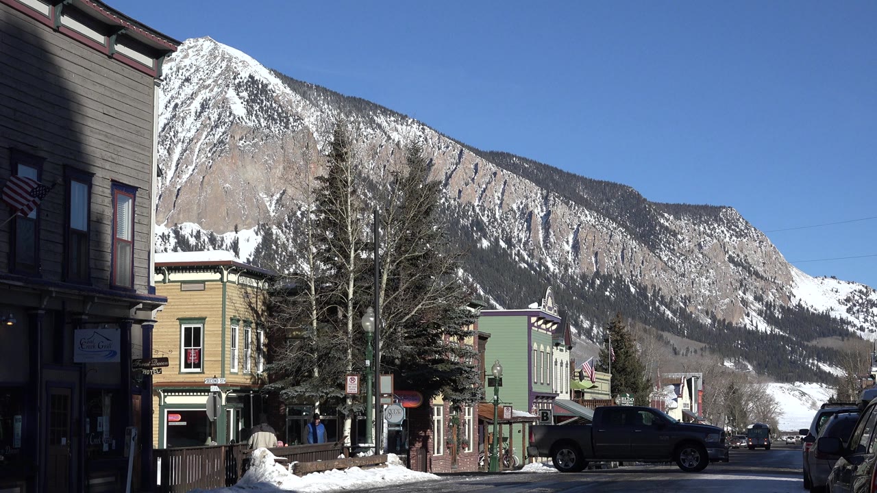 Snowy town street with storefronts below a large mountain