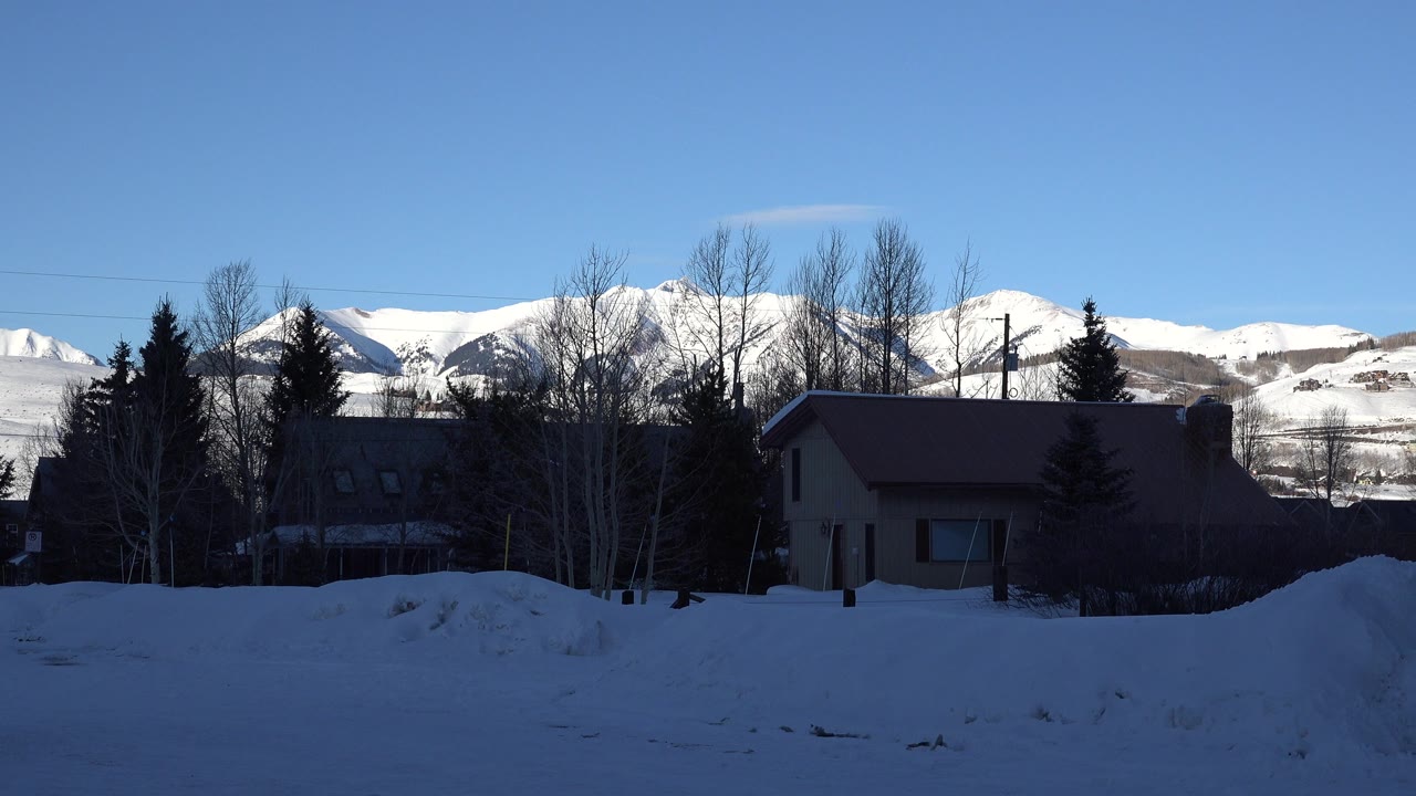 Snowy houses and bare trees below sunlit mountains