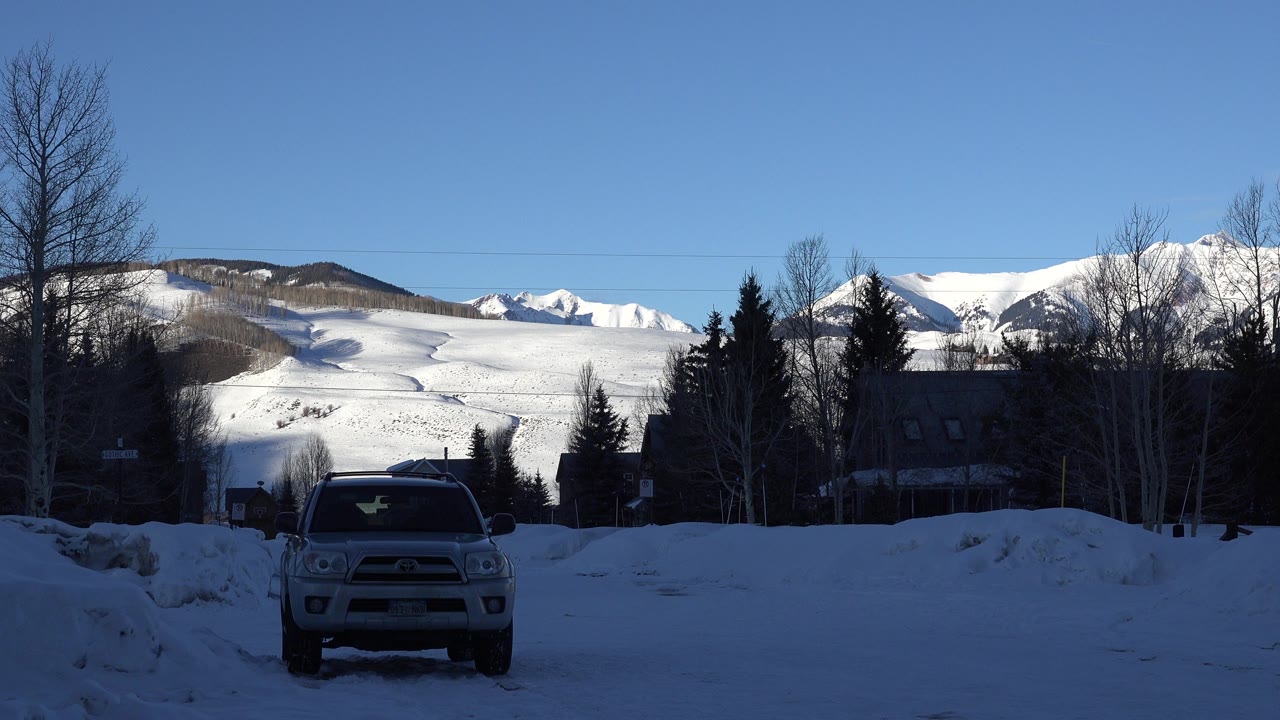 Parked SUV on a snowy road with mountains and trees behind it