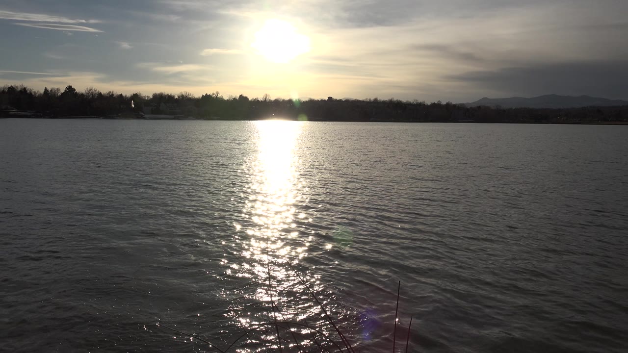 Lake horizon with sun glare, shoreline, and lens flare.