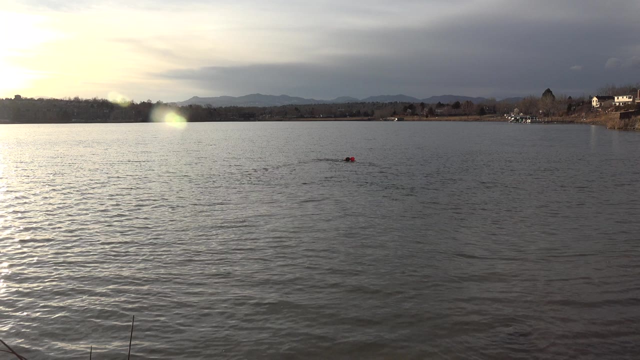 Distant small object moving across a rippled lake under a cloudy bright sky.