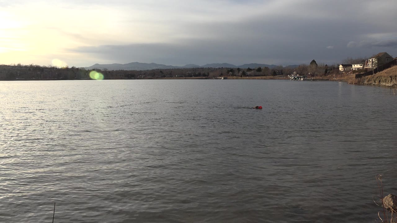 Red object floating on rippled water below a cloudy sky.