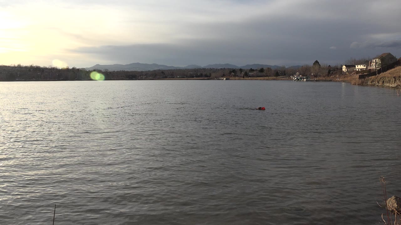 The red object remains on the open water in Westminster, Colorado, while bright glare breaks through clouds above distant hills and no people are visible.