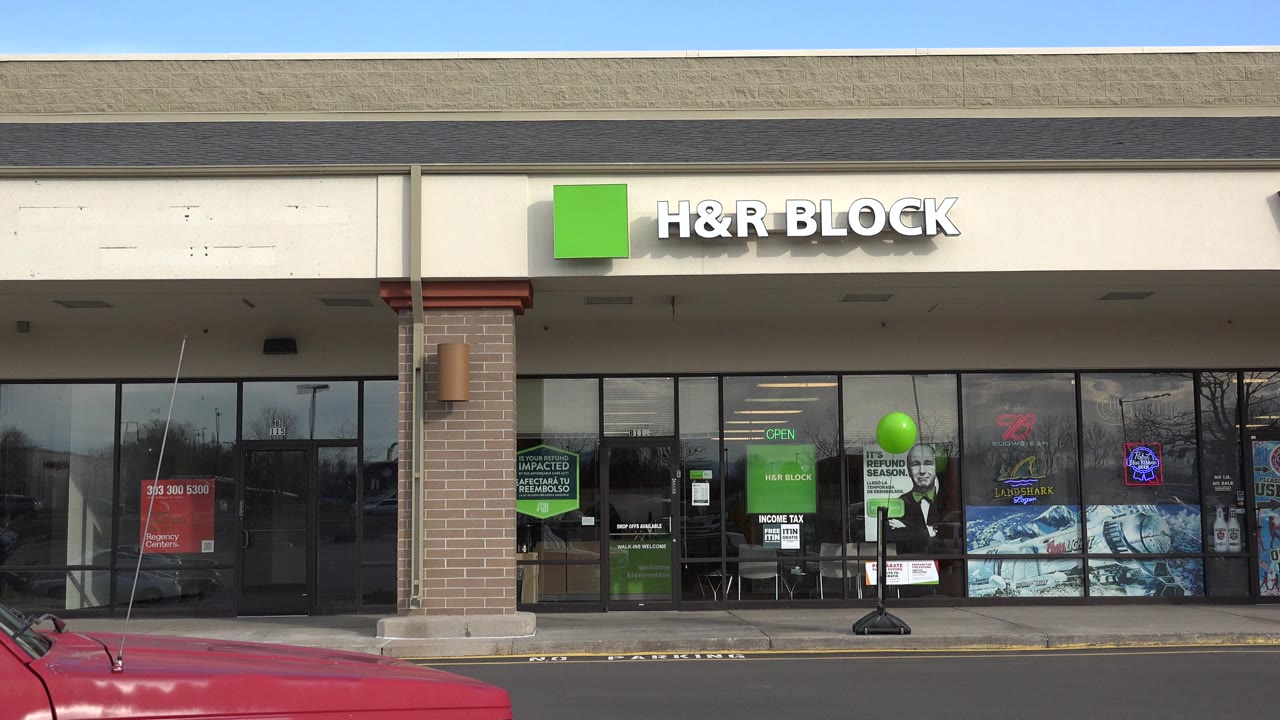 Second frame holds on the Westminster H&R Block exterior, with the green balloon centered near the windows and the red pickup hood lower left, with no visible people.