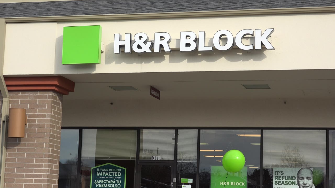 The storefront in Westminster, Colorado, shows the H&R Block sign across the top, dark window reflections below, a green balloon in front of the windows, and tax-season posters, with no visible people.