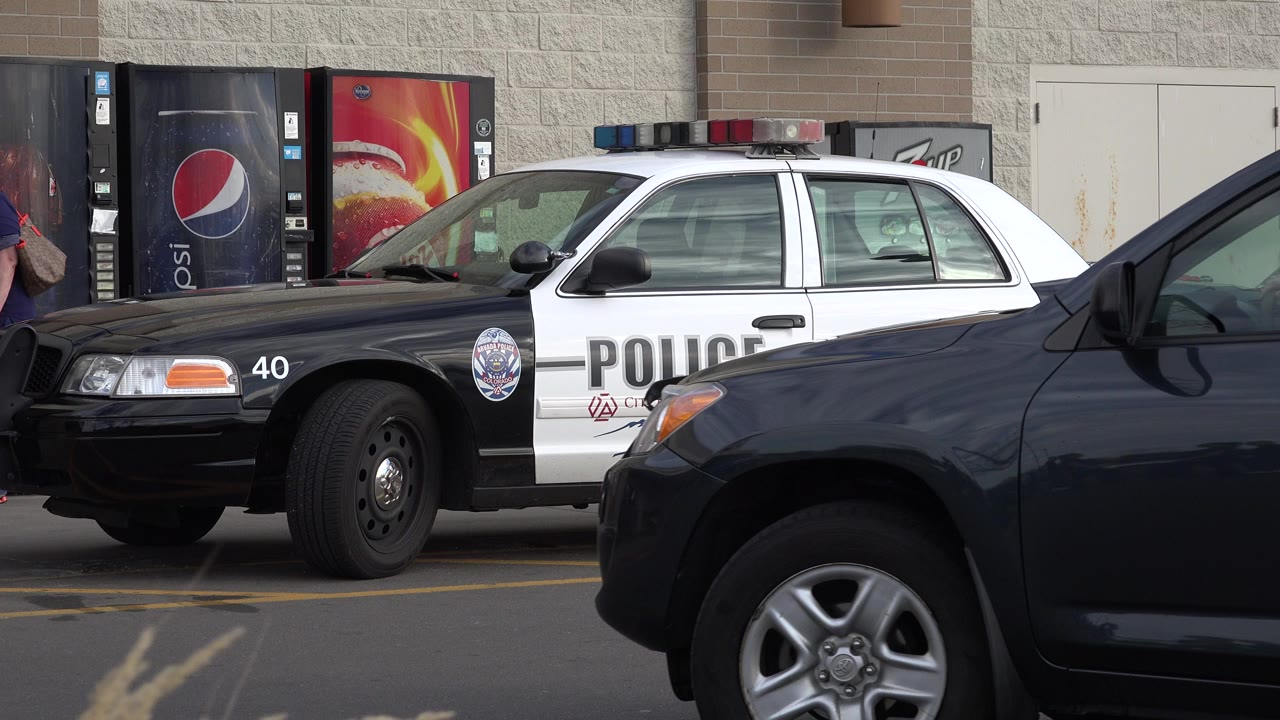 A parked black and white police car in Westminster, Colorado is partly obscured by a dark SUV passing in the foreground, with vending machines and a wall behind it.