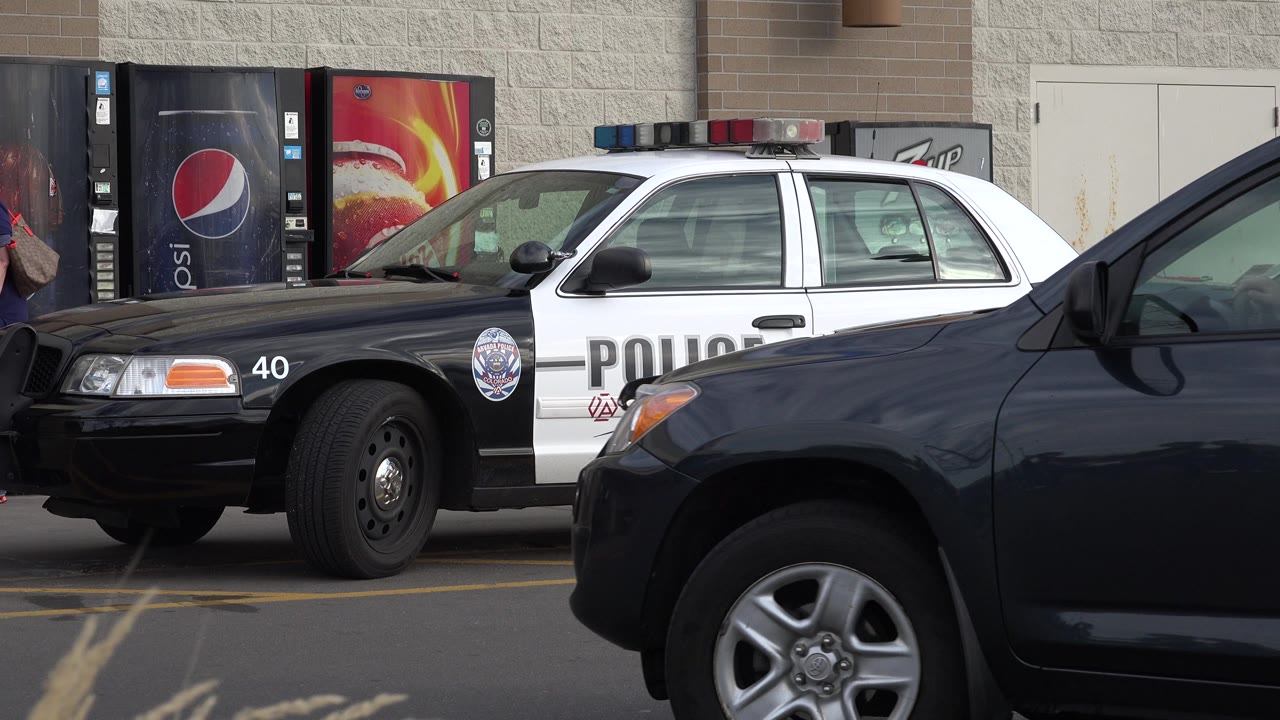 The dark SUV continues across the foreground in Westminster, Colorado, covering much of the parked police cruiser while soda vending machines remain visible behind it.