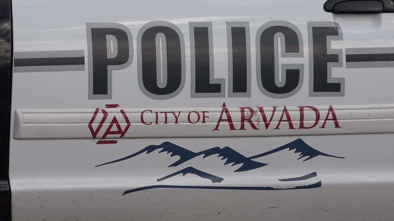 At 0:01, the close frame remains on the white police vehicle side in Westminster, Colorado, with the POLICE wordmark centered above City of Arvada text and a blue mountain graphic, with no visible people.