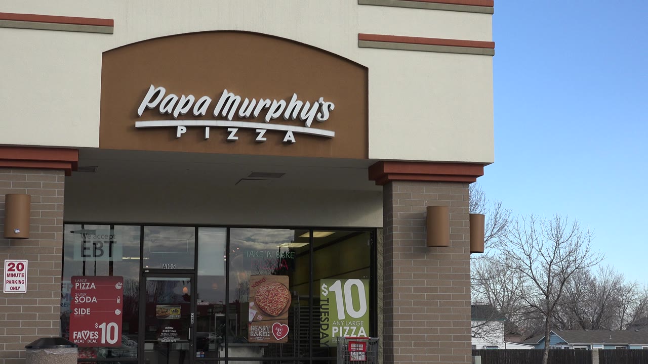 The Westminster storefront remains centered, with the Papa Murphy's sign, entrance doors, sale posters, sidewalk, bare trees, and suburban homes visible beyond the right side.