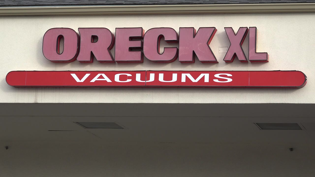 Opening frame of the Oreck XL Vacuums sign on a beige Westminster, Colorado storefront facade, with shaded awning below and no visible people.
