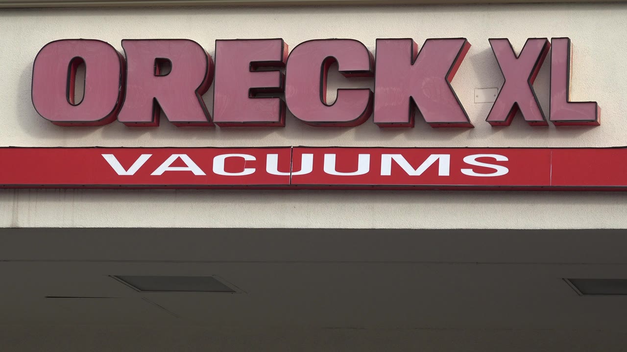 Close view of the red Oreck XL Vacuums storefront sign in Westminster, Colorado, with beige wall panels and no visible people.
