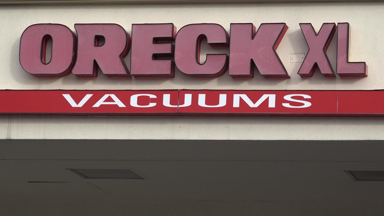 Centered view of the Oreck XL letters and red VACUUMS band on a beige commercial facade in Westminster, Colorado, with no visible people.