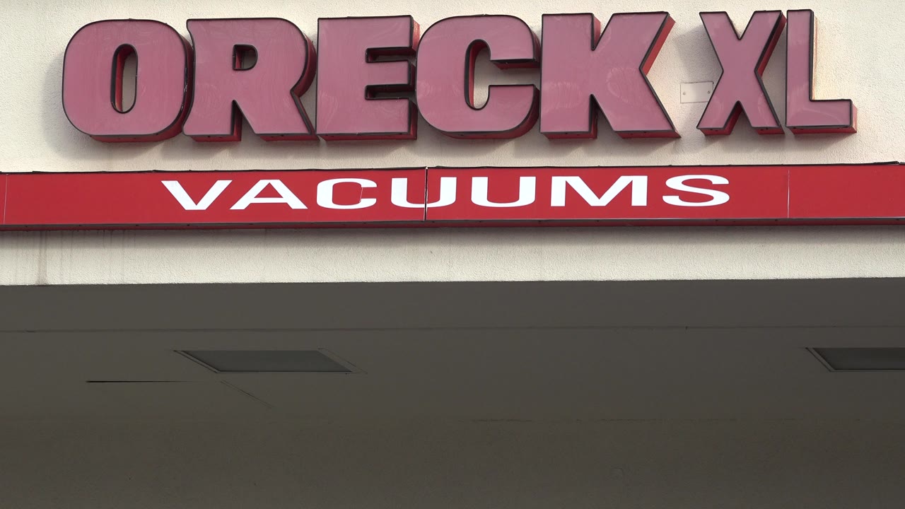 Close crop of the red Oreck XL Vacuums sign on a cream storefront fascia in Westminster, Colorado, with no visible people.
