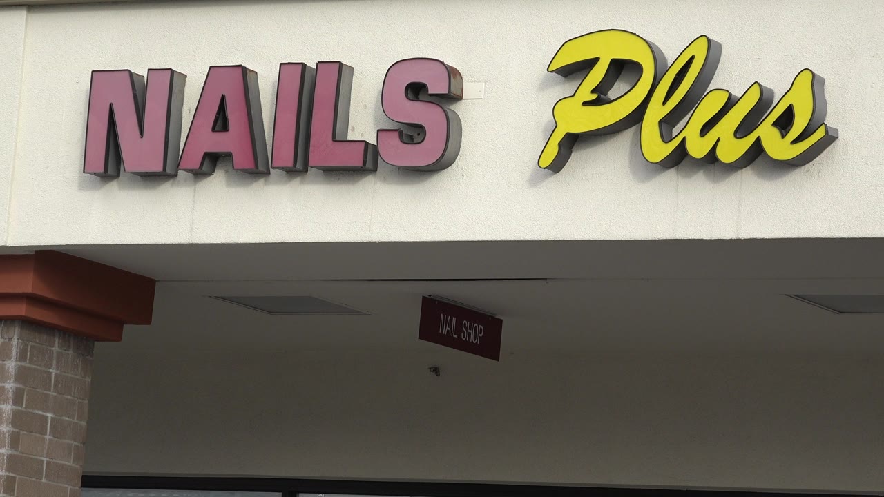 Tight view of the Nails Plus sign on a cream strip mall facade in Westminster, Colorado, with a covered walkway below and no visible people.